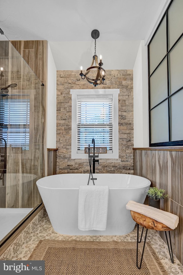 bathroom featuring a notable chandelier, a bathing tub, and tile walls