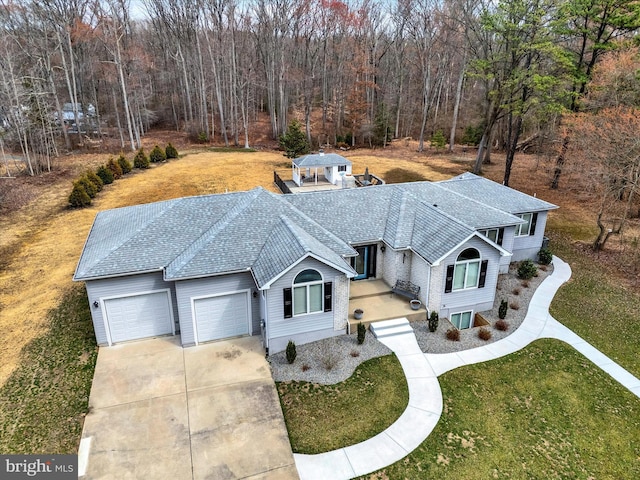 view of front of home featuring a front lawn, driveway, a wooded view, roof with shingles, and a garage