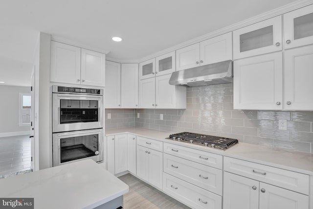 kitchen with appliances with stainless steel finishes, white cabinets, backsplash, light wood-type flooring, and light stone counters