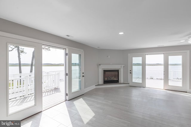 unfurnished living room with ceiling fan, a water view, and a healthy amount of sunlight