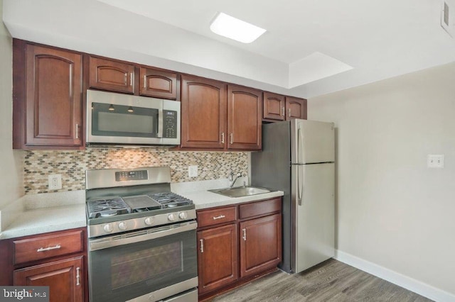 kitchen with appliances with stainless steel finishes, backsplash, hardwood / wood-style floors, and sink