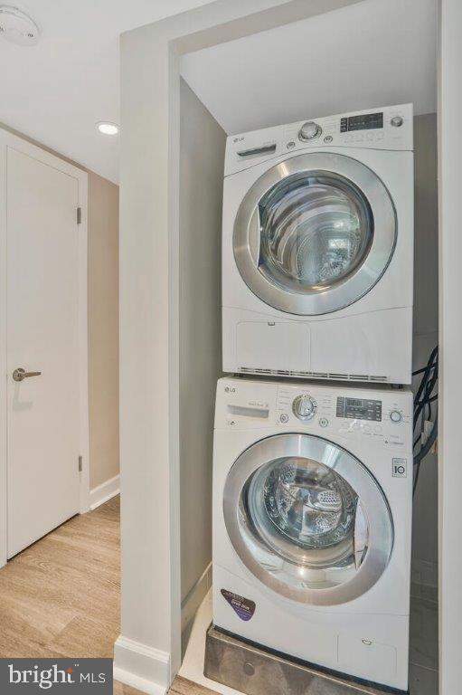 laundry area featuring stacked washer / dryer and light hardwood / wood-style flooring