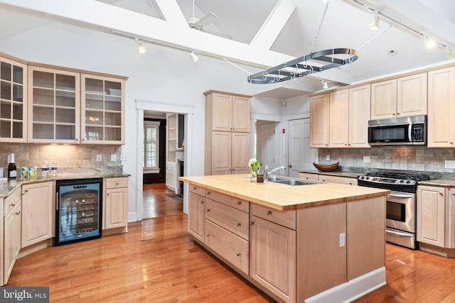 kitchen featuring light wood-type flooring, stainless steel appliances, wine cooler, a kitchen island with sink, and butcher block countertops