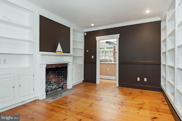 unfurnished living room featuring crown molding, built in shelves, and light hardwood / wood-style flooring