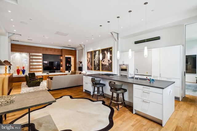 kitchen featuring decorative light fixtures, light hardwood / wood-style floors, sink, an island with sink, and white cabinets