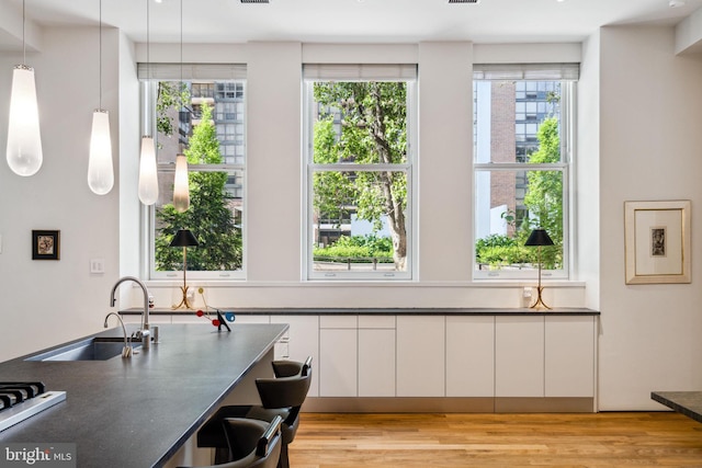 interior space with decorative light fixtures, white cabinets, light wood-type flooring, and a healthy amount of sunlight