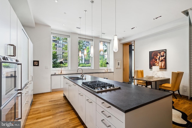 kitchen featuring white cabinets, hanging light fixtures, light hardwood / wood-style floors, and a kitchen island with sink