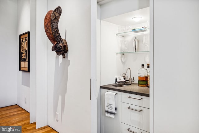 bar with white cabinets, sink, and light wood-type flooring