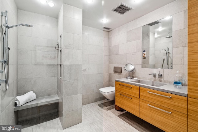 bathroom with tile walls, toilet, a tile shower, and vanity