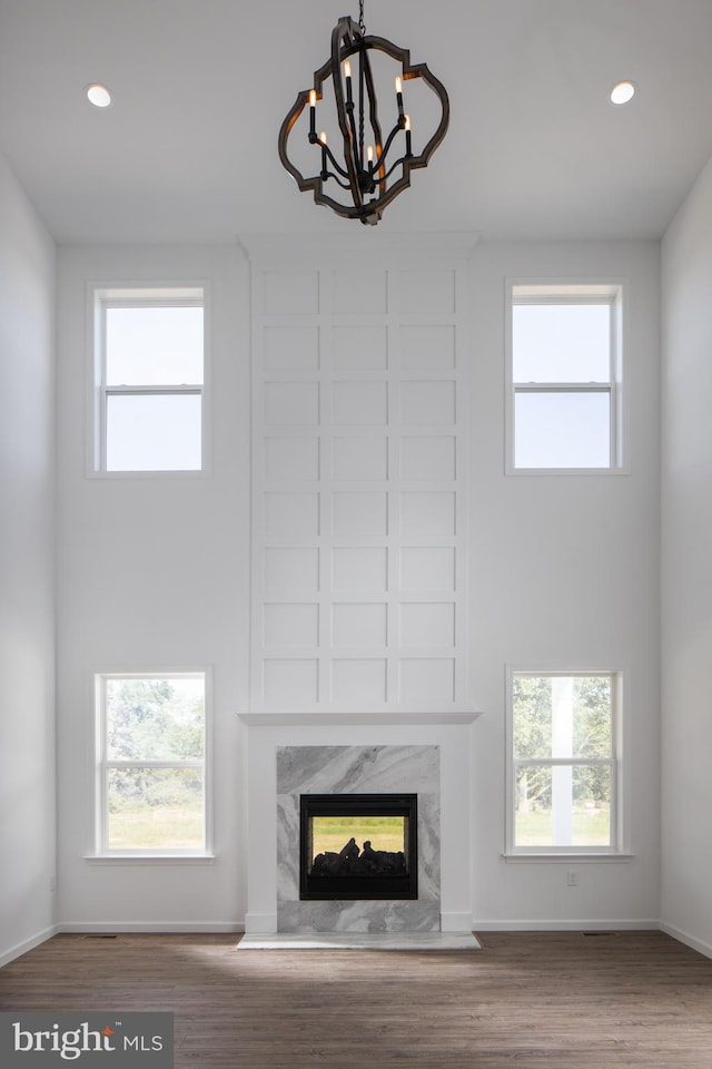 unfurnished living room featuring a towering ceiling, wood-type flooring, a fireplace, and a notable chandelier