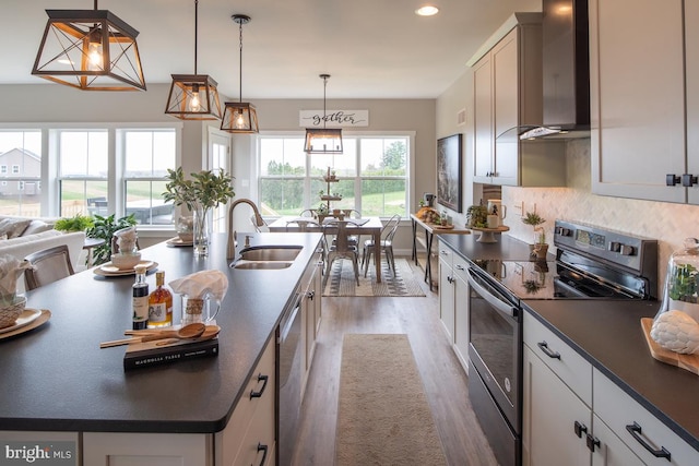 kitchen with sink, stainless steel appliances, white cabinets, wall chimney exhaust hood, and pendant lighting