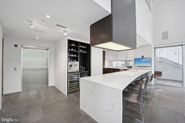 kitchen with a breakfast bar, track lighting, wine cooler, light stone counters, and white cabinetry