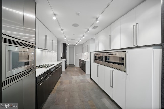 kitchen with rail lighting, tasteful backsplash, stainless steel appliances, sink, and white cabinetry