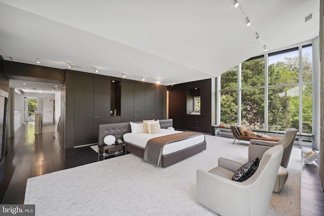 bedroom featuring lofted ceiling, rail lighting, dark hardwood / wood-style floors, and a wall of windows