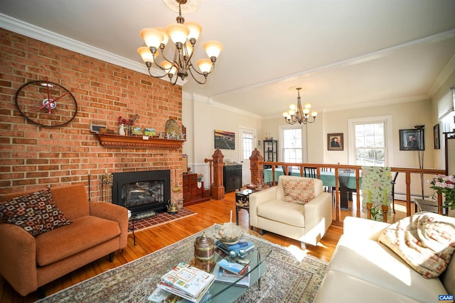 living room with brick wall, a brick fireplace, crown molding, an inviting chandelier, and light wood-type flooring