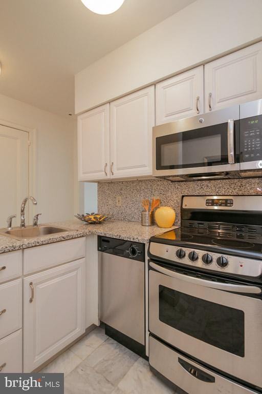 kitchen featuring white cabinets, stainless steel appliances, light stone countertops, sink, and light tile flooring