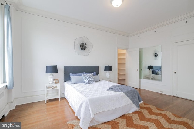 bedroom featuring a spacious closet, light hardwood / wood-style flooring, and crown molding