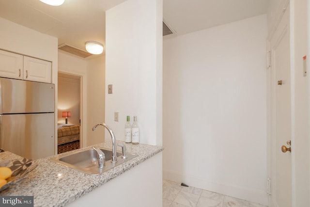 kitchen featuring stainless steel fridge, sink, light tile floors, white cabinets, and light stone countertops