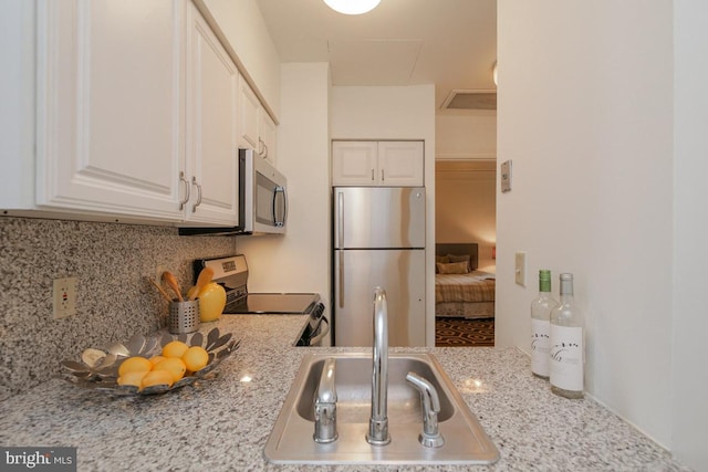 kitchen featuring appliances with stainless steel finishes, tasteful backsplash, white cabinets, light stone countertops, and sink