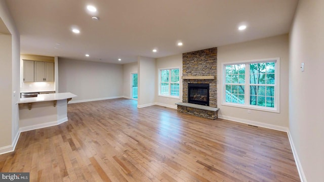 unfurnished living room with light wood finished floors, recessed lighting, visible vents, a stone fireplace, and baseboards
