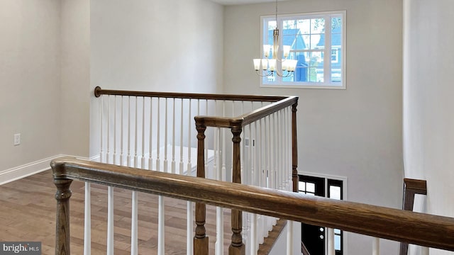 staircase with baseboards, wood finished floors, and a notable chandelier