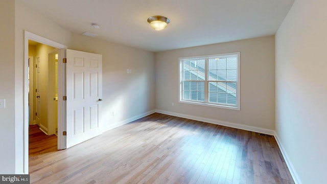 empty room featuring wood finished floors, visible vents, and baseboards
