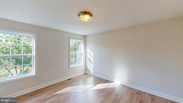 empty room with wood-type flooring, visible vents, and baseboards