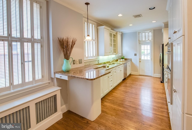 kitchen featuring decorative light fixtures, a healthy amount of sunlight, white cabinetry, and light hardwood / wood-style flooring