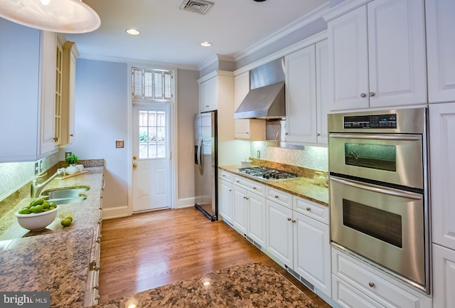 kitchen featuring tasteful backsplash, wall chimney range hood, stainless steel appliances, white cabinetry, and light hardwood / wood-style flooring