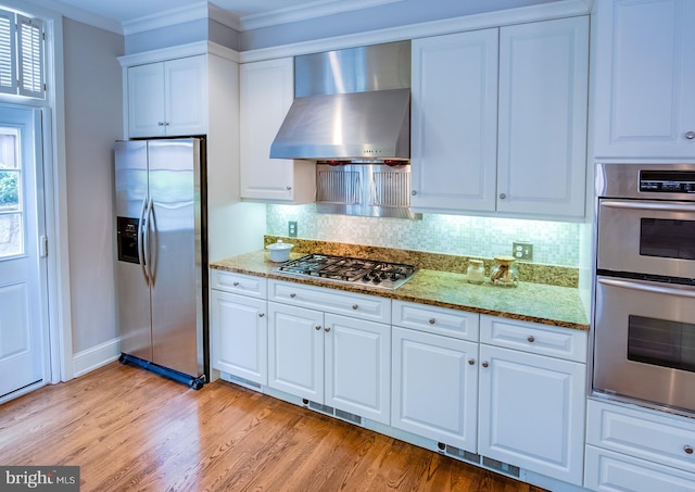 kitchen with appliances with stainless steel finishes, backsplash, wall chimney range hood, and white cabinetry