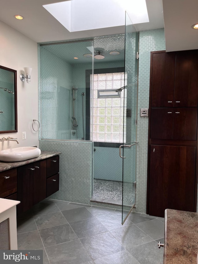 bathroom with a shower with shower door, a skylight, ceiling fan, vanity, and tile floors