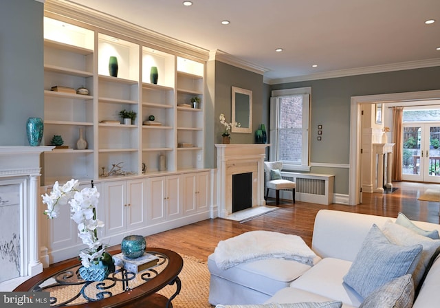 living room with french doors, built in shelves, ornamental molding, radiator, and light hardwood / wood-style flooring