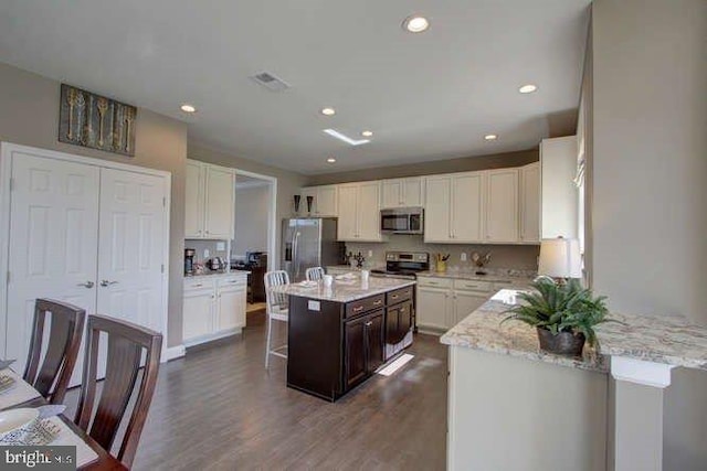 kitchen with dark hardwood / wood-style floors, a kitchen island, appliances with stainless steel finishes, light stone countertops, and dark brown cabinetry