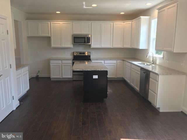 kitchen featuring dark wood-type flooring, stainless steel appliances, a center island, light stone countertops, and sink