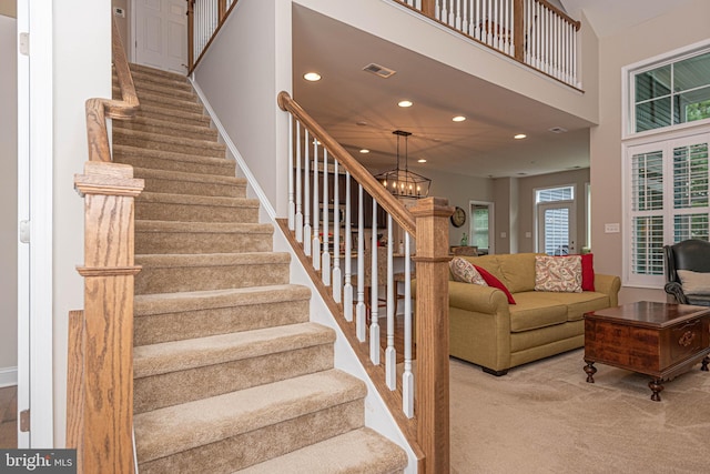 stairs featuring an inviting chandelier, a high ceiling, and carpet