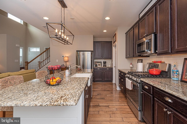 kitchen with a chandelier, an island with sink, light hardwood / wood-style flooring, appliances with stainless steel finishes, and dark brown cabinetry