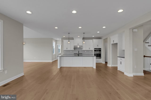 kitchen with pendant lighting, a center island with sink, sink, light hardwood / wood-style floors, and white cabinetry