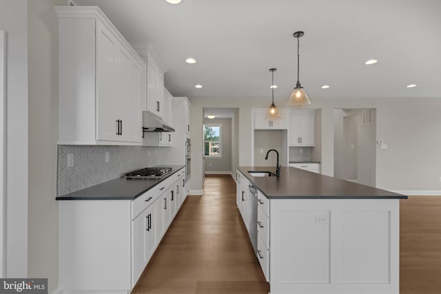 kitchen with white cabinetry, sink, hanging light fixtures, a kitchen island with sink, and light wood-type flooring