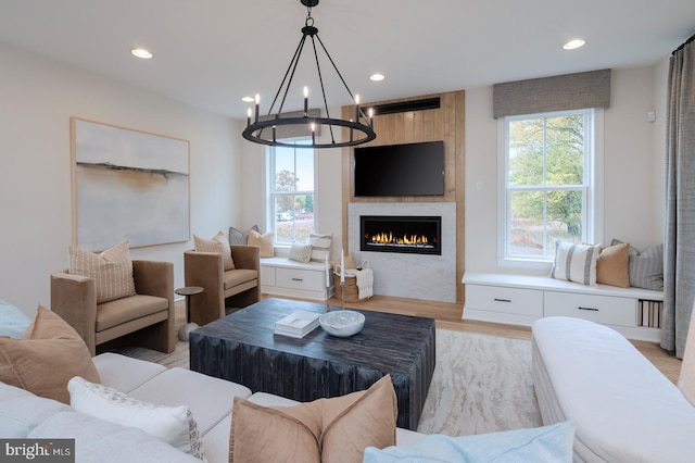 living room with a large fireplace, light hardwood / wood-style flooring, a healthy amount of sunlight, and a notable chandelier