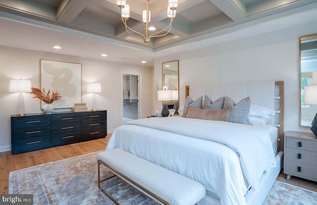 bedroom with beam ceiling, coffered ceiling, a notable chandelier, light hardwood / wood-style floors, and a walk in closet