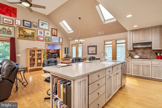 kitchen featuring a skylight, ceiling fan with notable chandelier, light hardwood / wood-style floors, sink, and a center island with sink