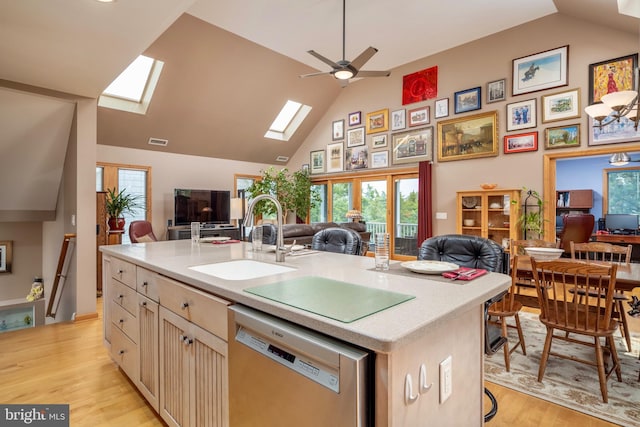 kitchen with a kitchen island with sink, sink, a skylight, stainless steel dishwasher, and light hardwood / wood-style floors