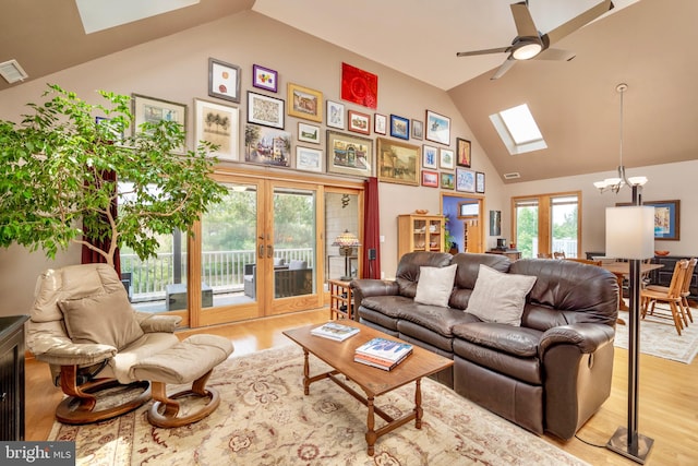 living room with high vaulted ceiling, a skylight, french doors, ceiling fan with notable chandelier, and light hardwood / wood-style flooring