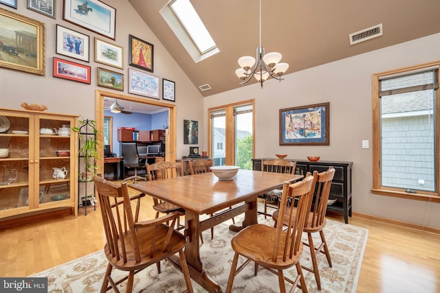 dining space featuring high vaulted ceiling, ceiling fan with notable chandelier, a skylight, and light wood-type flooring