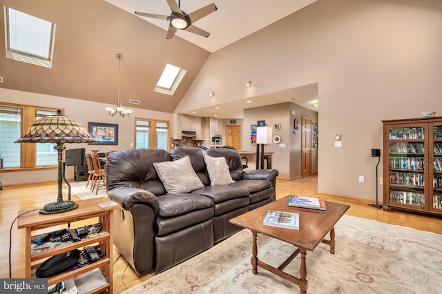 living room featuring a skylight, high vaulted ceiling, ceiling fan with notable chandelier, and light hardwood / wood-style flooring