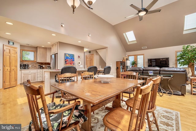 dining area featuring ceiling fan, high vaulted ceiling, light hardwood / wood-style floors, and a skylight