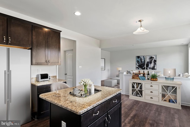 kitchen featuring dark hardwood / wood-style floors, light stone counters, high quality fridge, decorative light fixtures, and a center island