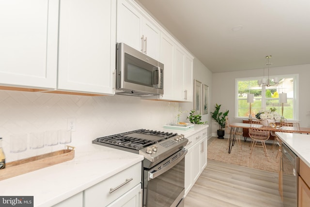 kitchen with stainless steel appliances, decorative light fixtures, a notable chandelier, light hardwood / wood-style floors, and white cabinetry