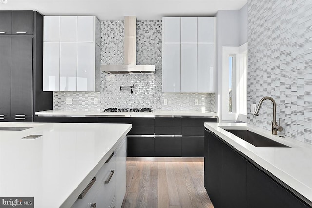 kitchen with white cabinetry, sink, light hardwood / wood-style floors, and wall chimney range hood