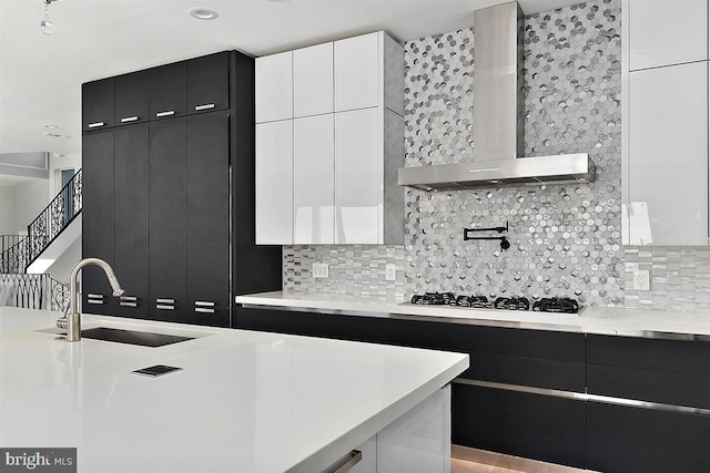 kitchen with white cabinets, sink, backsplash, and wall chimney range hood